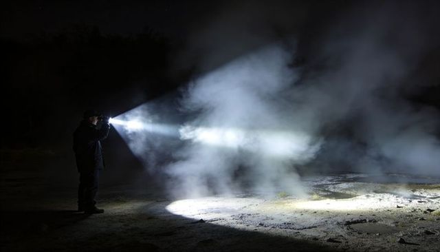 Solitary Man Holding Flashlight Cutting Through Fog at Night Over Damp Ground