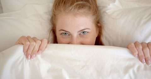 Red-Haired Young Woman Relaxing Under White Duvet in Bedroom