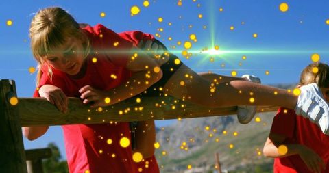 Child climbing wooden rail and swinging leg during sunny outdoor play with lens flare
