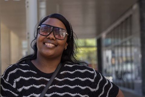 African woman smiling in oversized sunglasses standing in urban arcade with crossbody bag