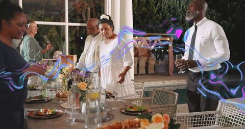 Adjusting mature woman in white dress reaching across elegant poolside dinner table at night