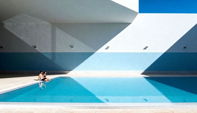 Couple sitting at minimalist poolside with dramatic sun and shadow geometry