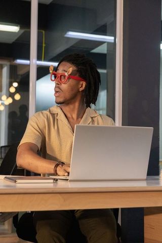 African american man wearing red novelty glasses working on laptop in coworking space