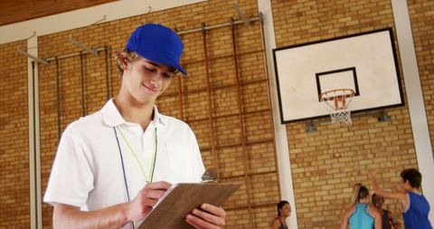 Basketball coach writing on clipboard in indoor court
