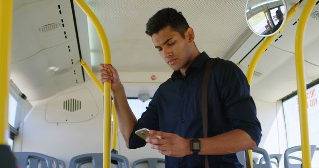 Focused biracial man standing on sunny city bus using smartphone. Communication, transport, city living and lifestyle, unaltered.