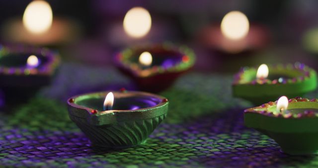 Lit candles in decorative clay pots on woven table mat, focus on foreground, bokeh background. diwali festival, celebration, tradition and ceremony concept.