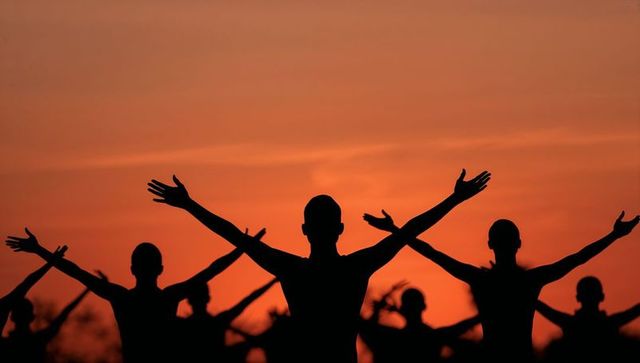 Silhouetted group stretching with arms raised at vibrant sunset for wellness and teamwork