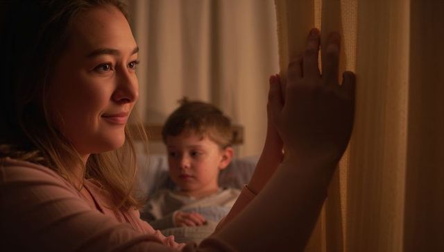 Young woman comforting child at night by window curtain, warm bedside caregiving moment