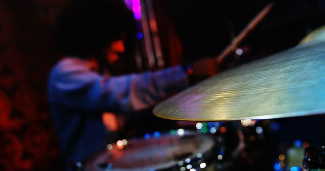 Dramatic shot capturing a drummer in the middle of a performance, with a sharp focus on the cymbal and a blurred background. Ideal for promoting live music events, music-focused blogs, or band promotions. Perfect to showcase the intensity and passion of live performances.