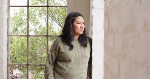 Thoughtful Woman Looking Out Bright Window with Foliage View