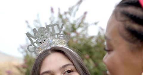 Friends chatting outdoors wearing merry christmas headband, festive holiday garden moment