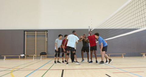 Diverse male volleyball team celebrating with high-fives in school gymnasium