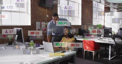 Colleagues collaborating on laptop in modern loft office surrounded by digital notifications