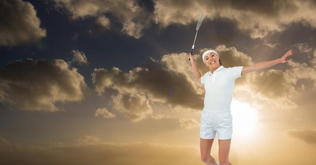 This image showcases an energetic woman in mid-serve while playing tennis. The dramatic cloudy sky with an emerging sun in the background adds a dynamic and inspiring atmosphere. Perfect for use in sports promotions, motivational posters, and fitness advertisements, highlighting themes of determination and outdoor sports.