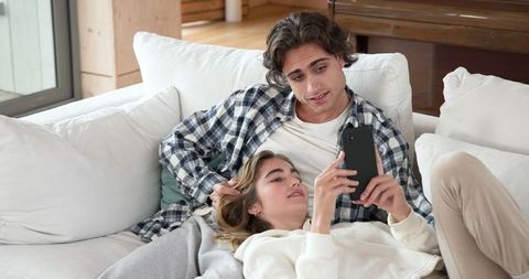 Relaxed Couple Using Smartphone on White Sofa at Home