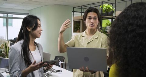 Coworkers discussing sustainability with tech devices in office