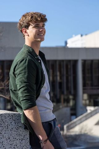 Young man leaning on concrete railing smiling and looking up casual urban campus lifestyle