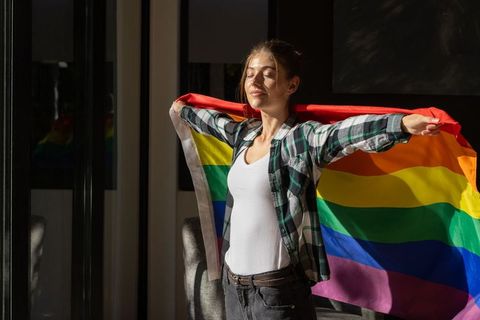 Proud Woman Holding Rainbow Flag in Sunlit Living Room