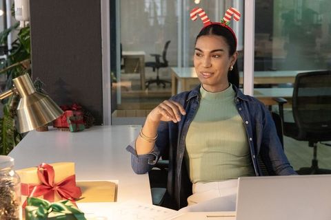 Office professional wearing candy-cane headband arranging holiday gifts at modern office