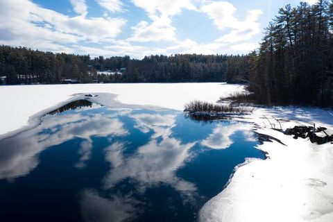 Melting winter lake reflecting bright blue sky and clouds beside snow-covered pine forest