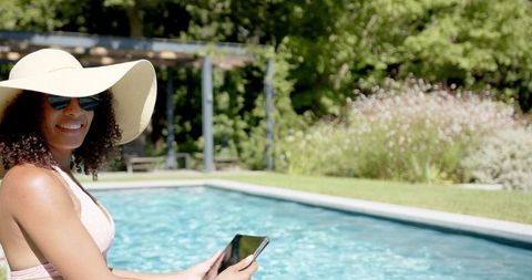 Woman Relaxing Poolside with Tablet and Sunhat on Summer Day