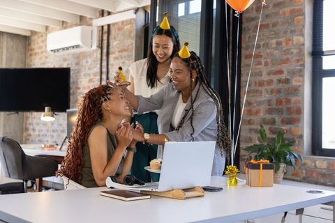 Diverse female coworkers celebrating office birthday with laughter and cupcakes