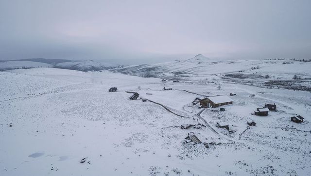Wooden farmhouse and cabins sitting on snowy plateau with winding track and solitude