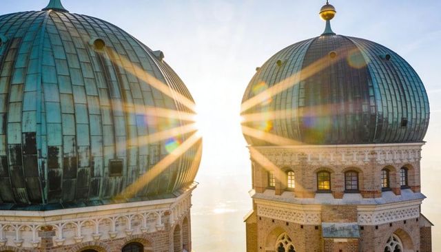 Twin patina copper domes with sunstar flare crowning ornate brick towers at sunrise