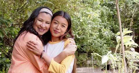 Smiling Mother and Daughter Embracing in Lush Backyard Garden