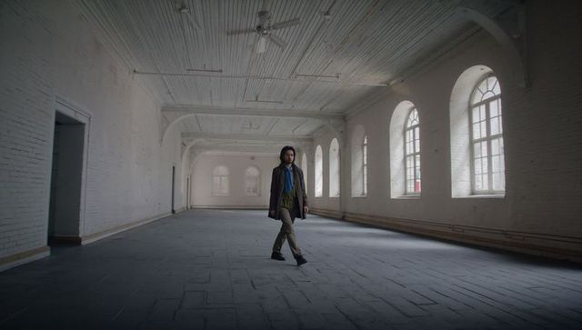 Solitary man walking through expansive industrial hall with arched windows and notebook