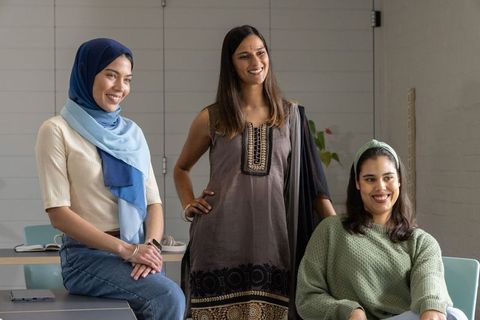 Diverse young women smiling and collaborating in modern classroom with laptop and hijab