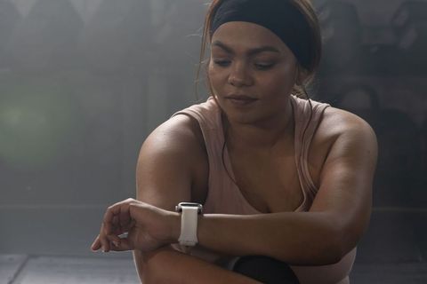 African american woman checking smartwatch after training, moody gym lighting