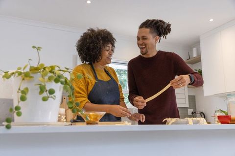 Couple making fresh pasta on kitchen island, laughing while stretching dough together