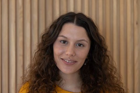 Smiling woman posing in mustard sweater against wooden slat wall warm friendly portrait