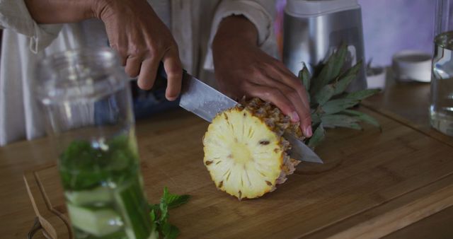 This close-up captures a person slicing a fresh pineapple on a wooden cutting board, showcasing the textures and details of the fruit. Suitable for use in articles, blogs, or advertisements related to cooking, healthy recipes, tropical fruit, or kitchen activities. Can also be used in promotional materials for cooking classes or kitchenware products.