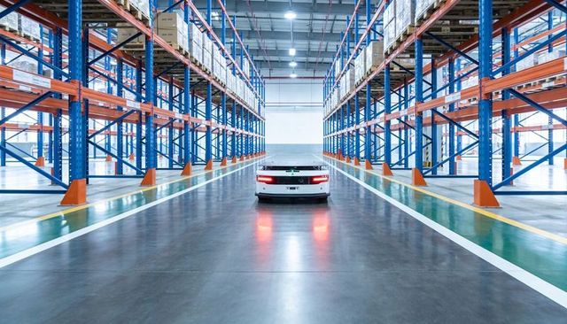 Autonomous agv navigating central aisle between pallet racking in modern distribution center