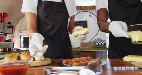 Preparing hot dogs with cheese and condiments, heart frame street food stall