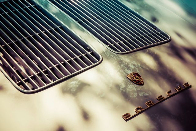 Features a close-up of a vintage Porsche car hood. Displays distinctive grille and iconic Porsche logo emblem. Ideal for use in automotive magazines, classic car collections, luxury brand advertisements, and retro-themed designs.