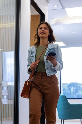 Confident african american professional walking into modern office holding smartphone