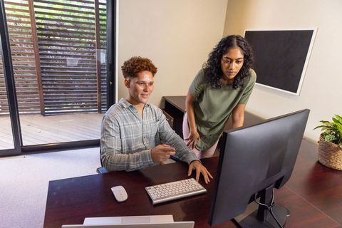 Diverse coworkers collaborating at office desk with desktop computer