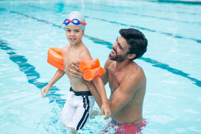 Father and son having fun together in a swimming pool. They are enjoying quality time, with the father helping his young son. Ideal for themes related to family bonding, summer activities, and childhood memories.