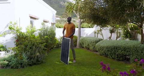Man Holding Solar Panel in Lush Garden: Embracing Green Energy
