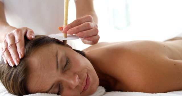 Woman experiencing ear candling therapy for stress relief and holistic healing. Ideal for promoting services in wellness spas, alternative medicine centers, and self-care guides.