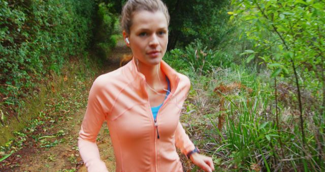 A young Caucasian woman is jogging on a forest trail, wearing athletic gear, with copy space. Her focused expression and active posture suggest a commitment to fitness and the enjoyment of nature during exercise.