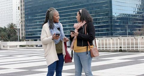 African American Senior Friends Chatting in Urban Plaza Holding Smartphones and Bags