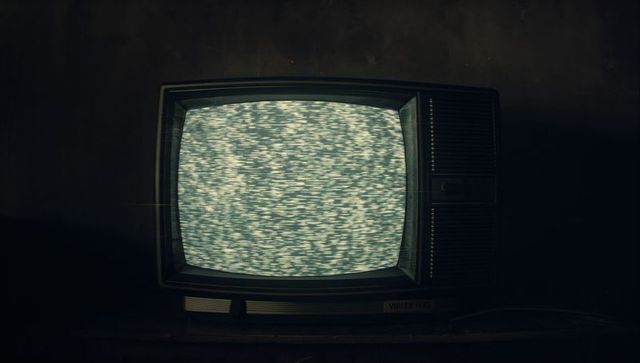 This image features a CRT television displaying static, evoking a strong sense of vintage nostalgia. The dim lighting and wooden table enhance the retro ambiance, suitable for themes relating to the past, memories, and media history. Perfect for use in creative projects exploring technology evolution, retro aesthetics, and antique electronics, or for backgrounds in film and TV set design.