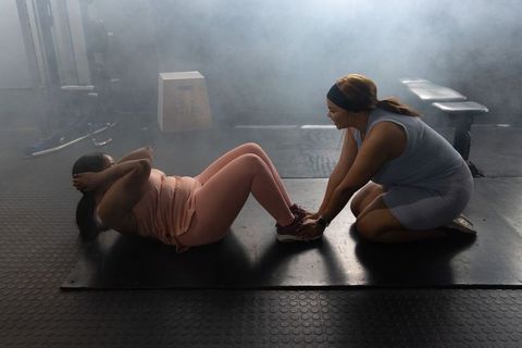 African american women doing partner sit-ups with trainer holding ankles for core strength