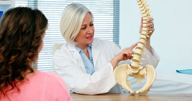 Female doctor is explaining spine model to patient in medical office. This is suitable for promoting healthcare facilities, medical education, spine health awareness, and patient care services.