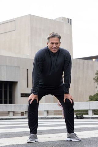 Senior man pausing during urban workout, checking smartwatch on striped concrete plaza