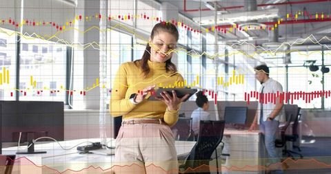 Businesswoman analyzing financial charts on tablet with stylus in modern open-plan office